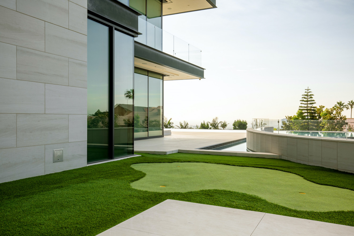 Private putting green overlooking the infinity-edge pool and panoramic Los Angeles views at a modern estate.