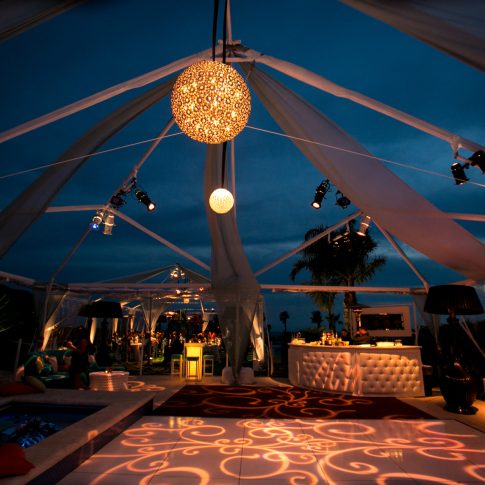 Malibu 40th birthday celebration with an illuminated dance floor built over the pool, open-air tenting, dramatic lighting, lounge seating, and a glowing bar.