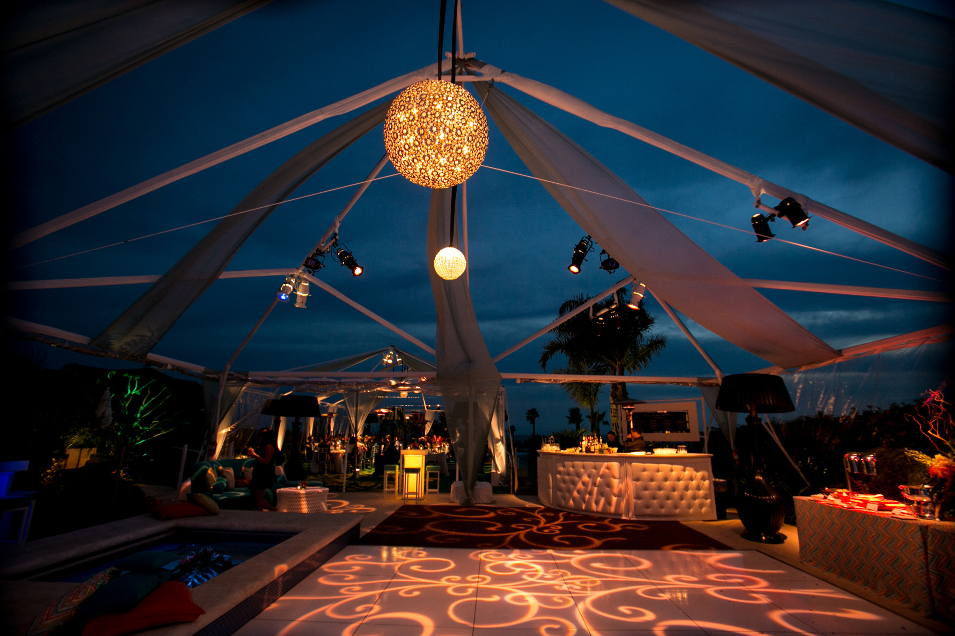 Malibu 40th birthday celebration with an illuminated dance floor built over the pool, open-air tenting, dramatic lighting, lounge seating, and a glowing bar.