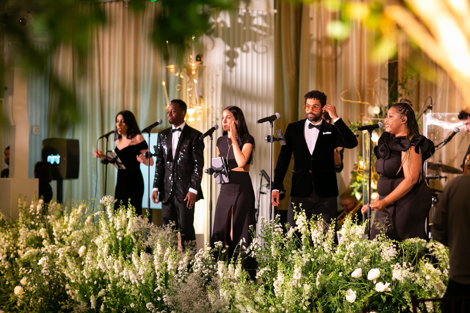Live band performing at an elegant private hotel event with formal black attire, lush white and green florals, and warm ambient lighting.