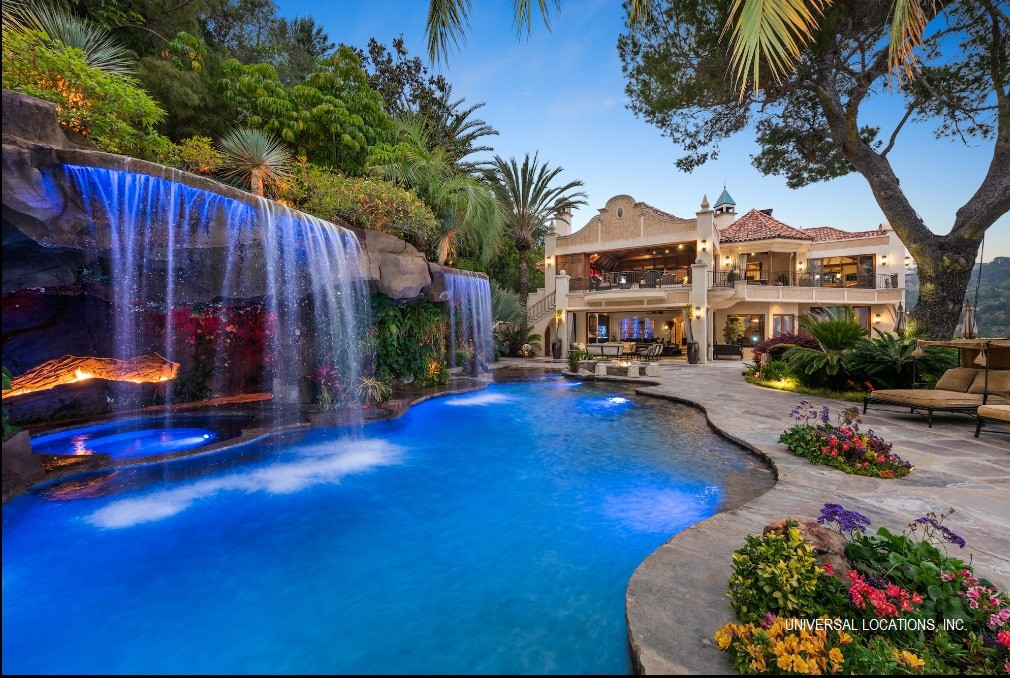 Resort-style swimming pool with dramatic waterfall, tropical landscaping, and panoramic city views.