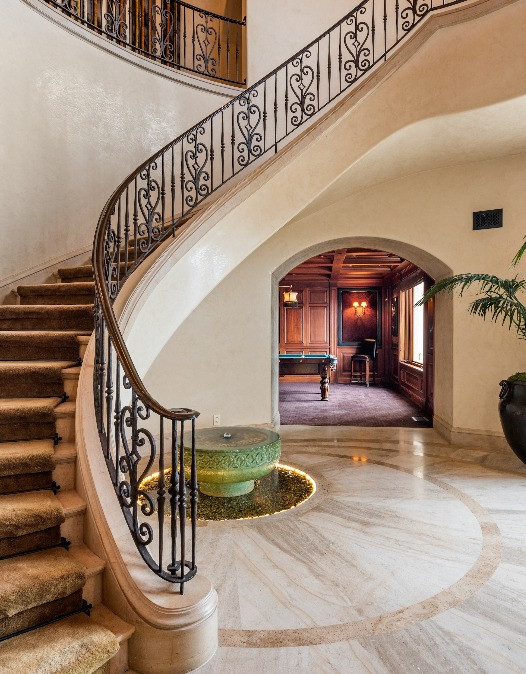 Elegant curved staircase with wrought-iron railing, marble flooring, and grand entry foyer inside a luxury Mediterranean estate.