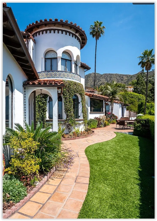 Landscaped garden pathway leading through a Spanish Revival estate with lush greenery and mountain views.