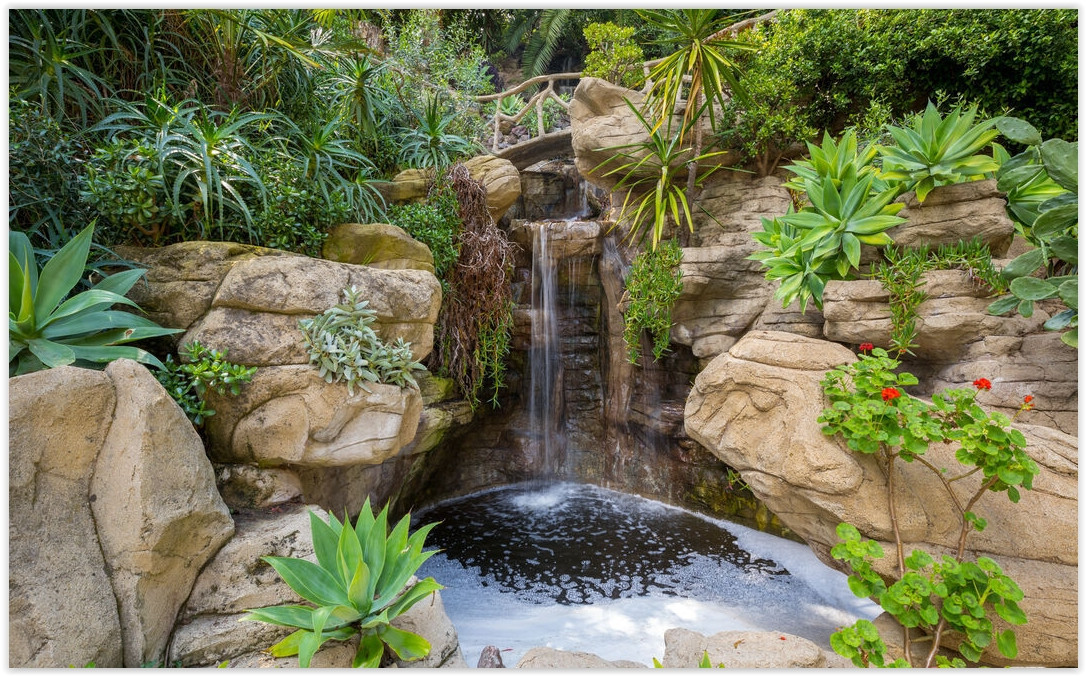 Natural rock waterfall surrounded by lush gardens and mature landscaping at a romantic Los Feliz private estate.