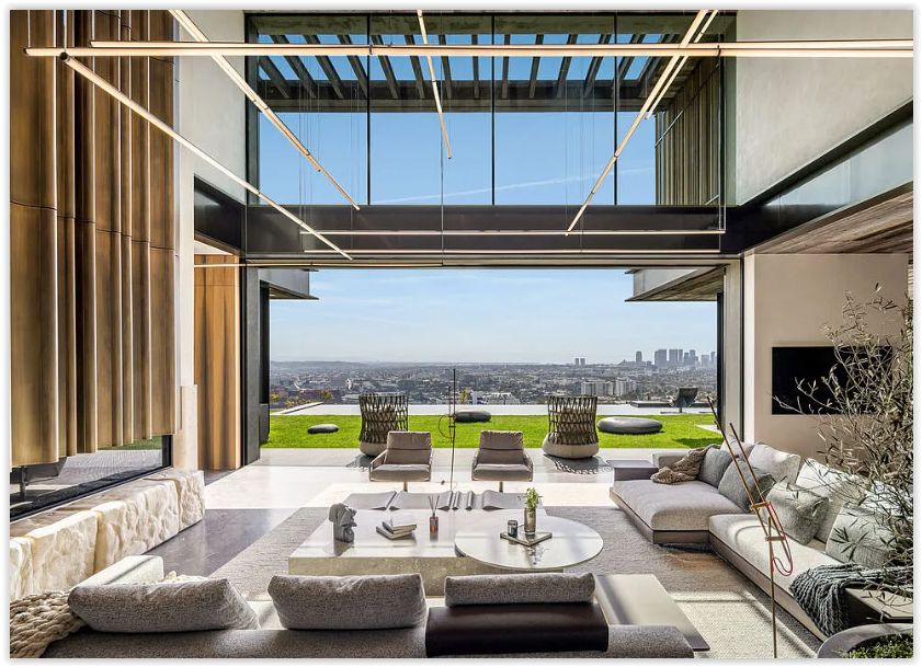 Modern living room with designer furnishings, a sculptural fire feature, floor-to-ceiling glass, and panoramic Los Angeles city views.