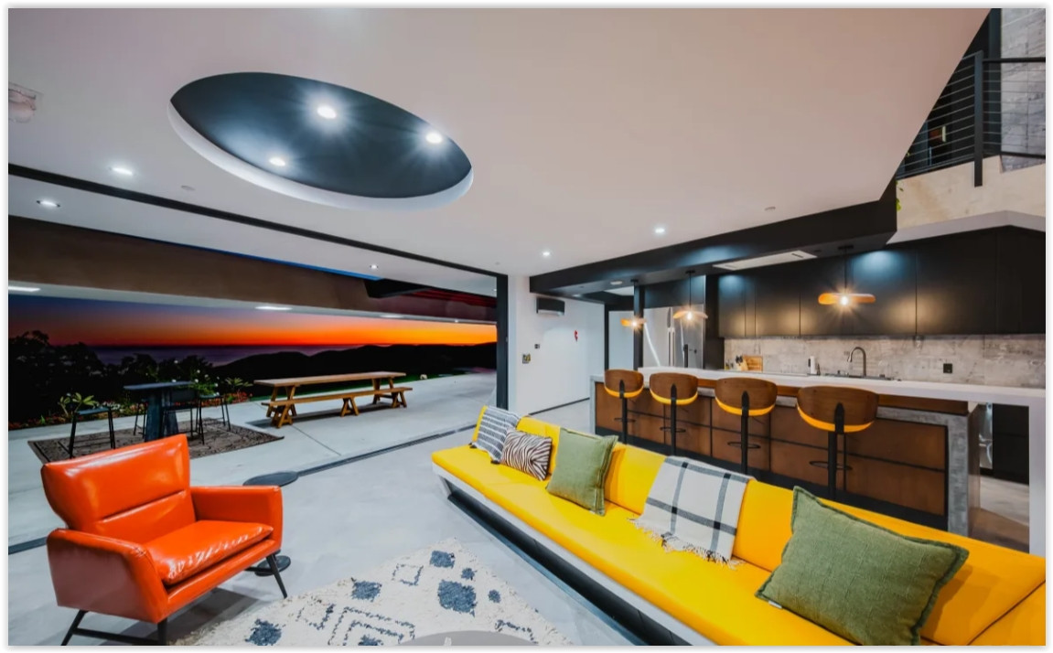 Open-concept living room and gourmet kitchen with floor-to-ceiling glass doors opening to panoramic Malibu sunset views.