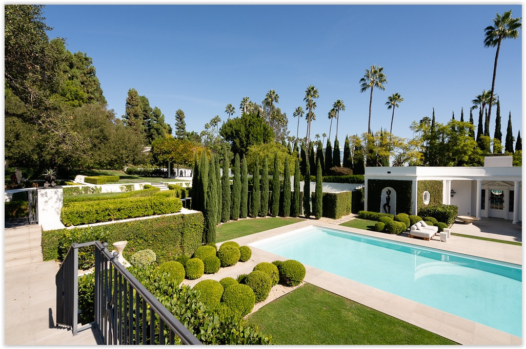 Italian cypress trees framing the resort-style pool and landscaped gardens of a luxury Beverly Hills estate.