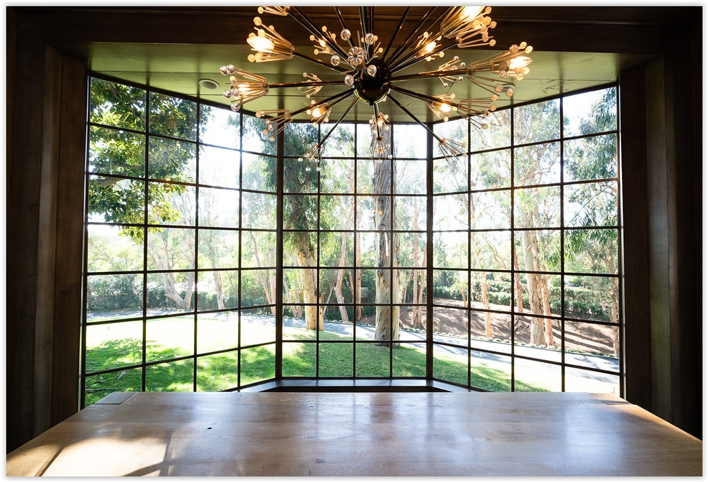 Floor-to-ceiling picture window overlooking the manicured gardens and mature trees of a Beverly Hills estate.