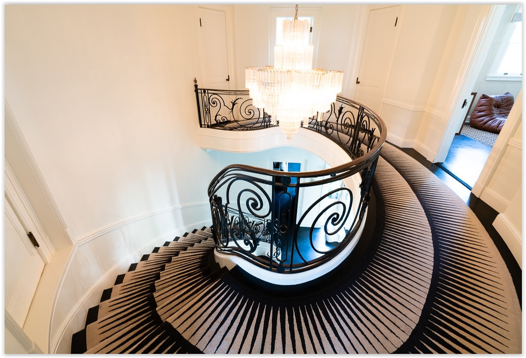 Elegant curved staircase with custom iron railing and crystal chandelier inside a classic Beverly Hills estate.