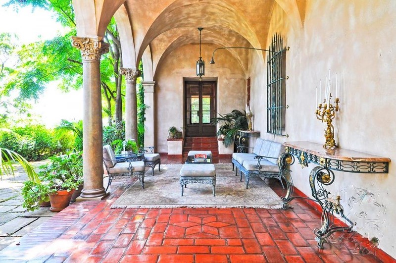Covered outdoor loggia with arched columns, terracotta flooring, and elegant seating overlooking the estate grounds.