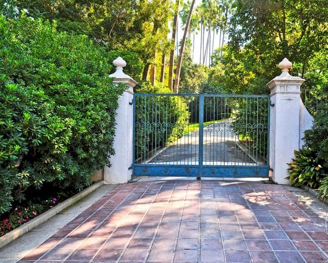 Private gated entrance with a tree-lined driveway leading to a secluded Spanish Colonial estate in Pasadena.