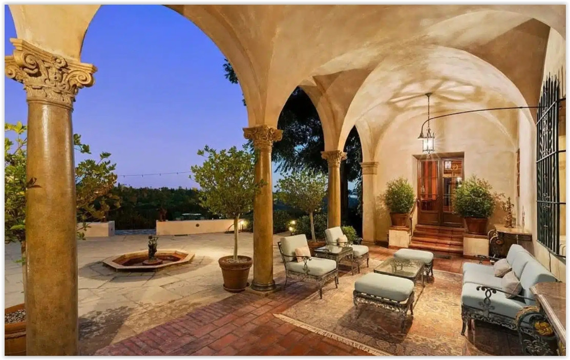 Covered Spanish Colonial loggia with arched columns, outdoor seating, and a fountain courtyard.