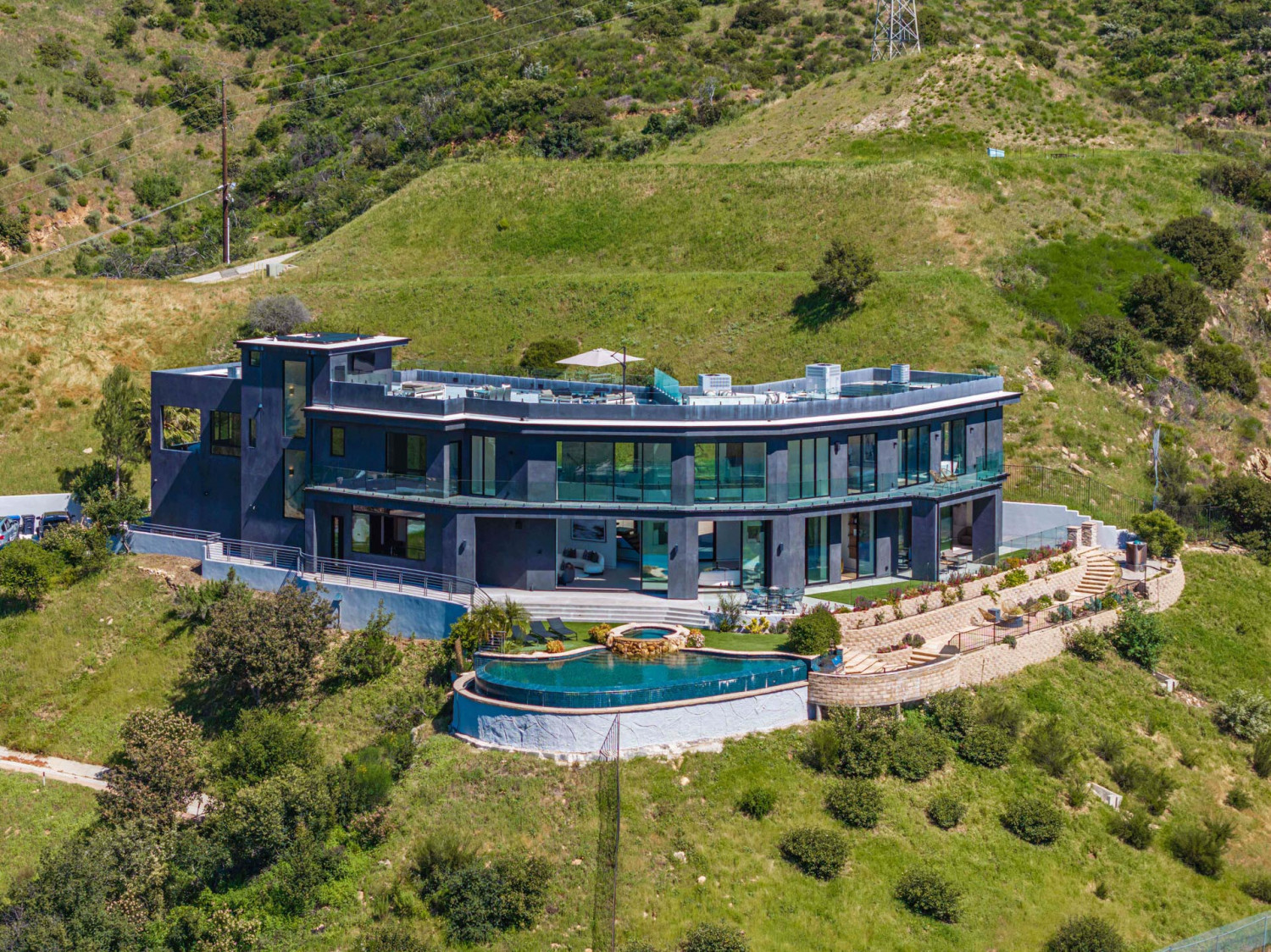 Aerial view of modern Agoura Hills estate set into hillside terrain, featuring resort-style pool, glass architecture, and surrounding canyon landscape in Los Angeles.