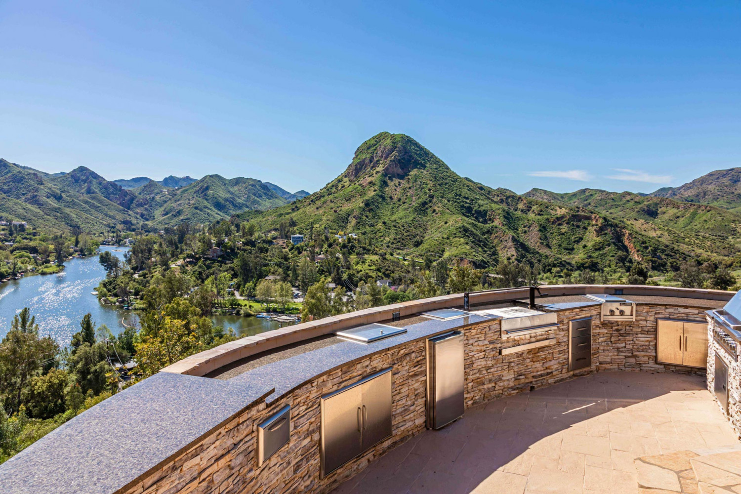 Outdoor kitchen and terrace at modern Agoura Hills estate overlooking lake and surrounding canyon landscape in Los Angeles.
