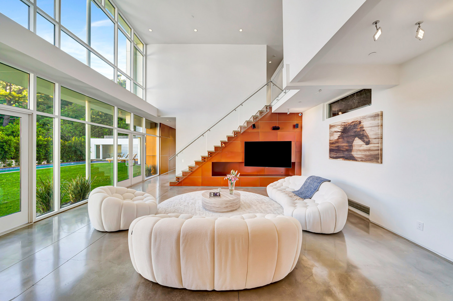 Contemporary living area with sculptural seating, glass walls, and seamless transition to outdoor pool and lawn area.