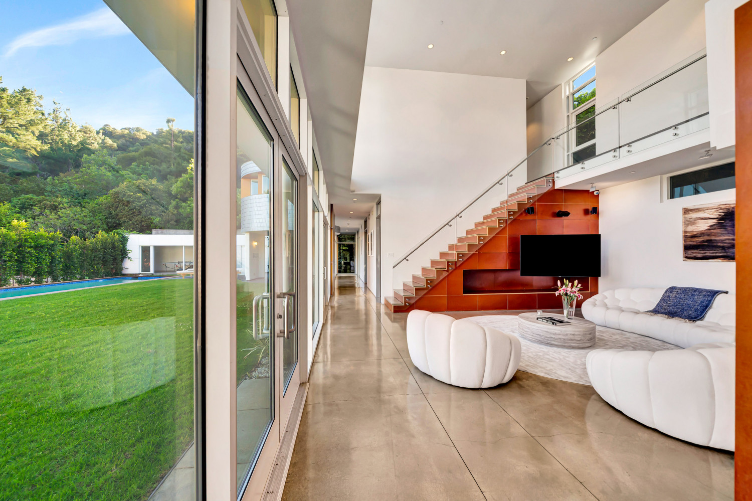 Contemporary living area with sculptural seating, glass walls, and seamless transition to outdoor pool and lawn area.