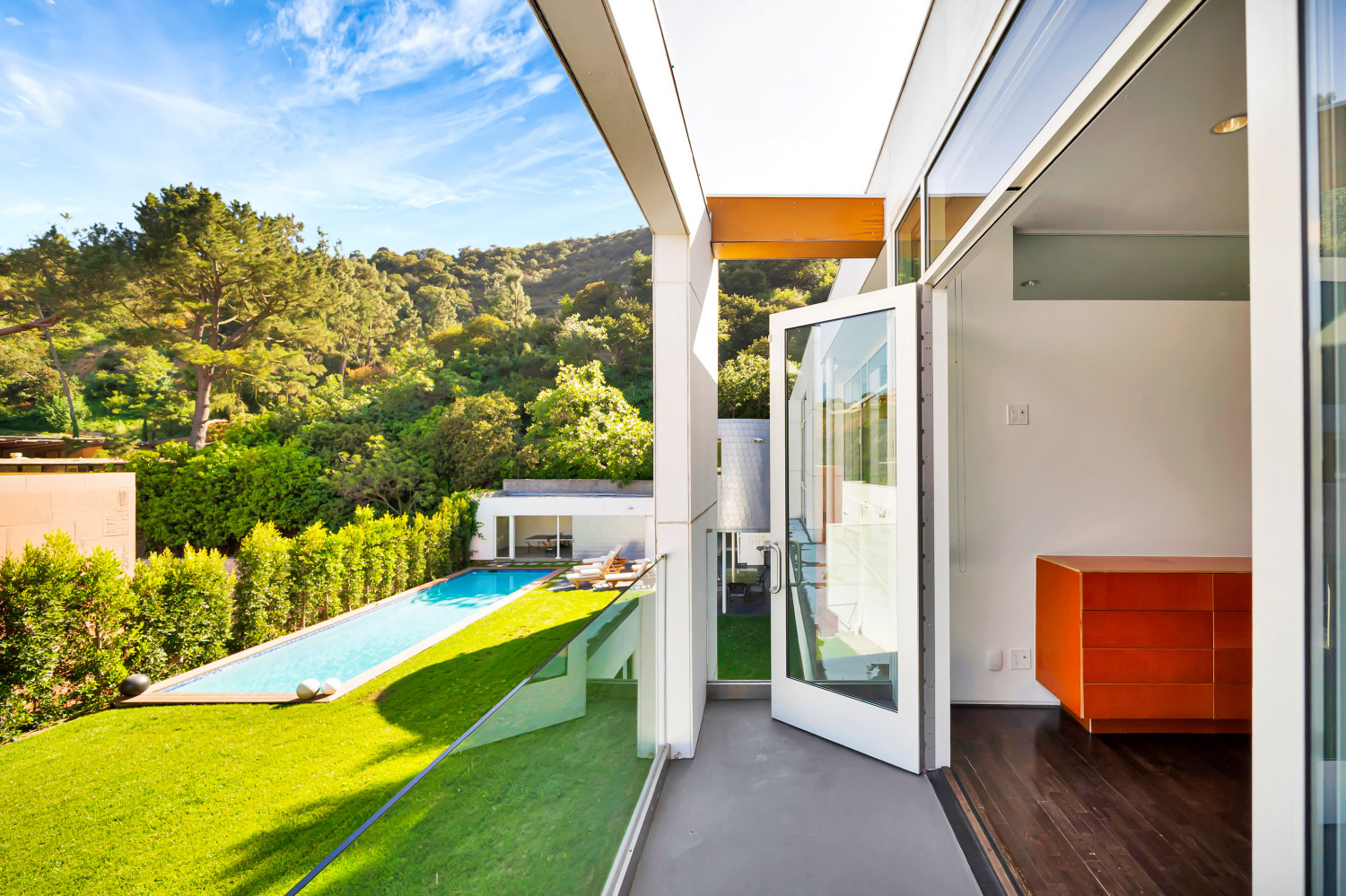 Open living room with modern seating, floor-to-ceiling glass doors, and direct views toward the pool and hillside landscape.