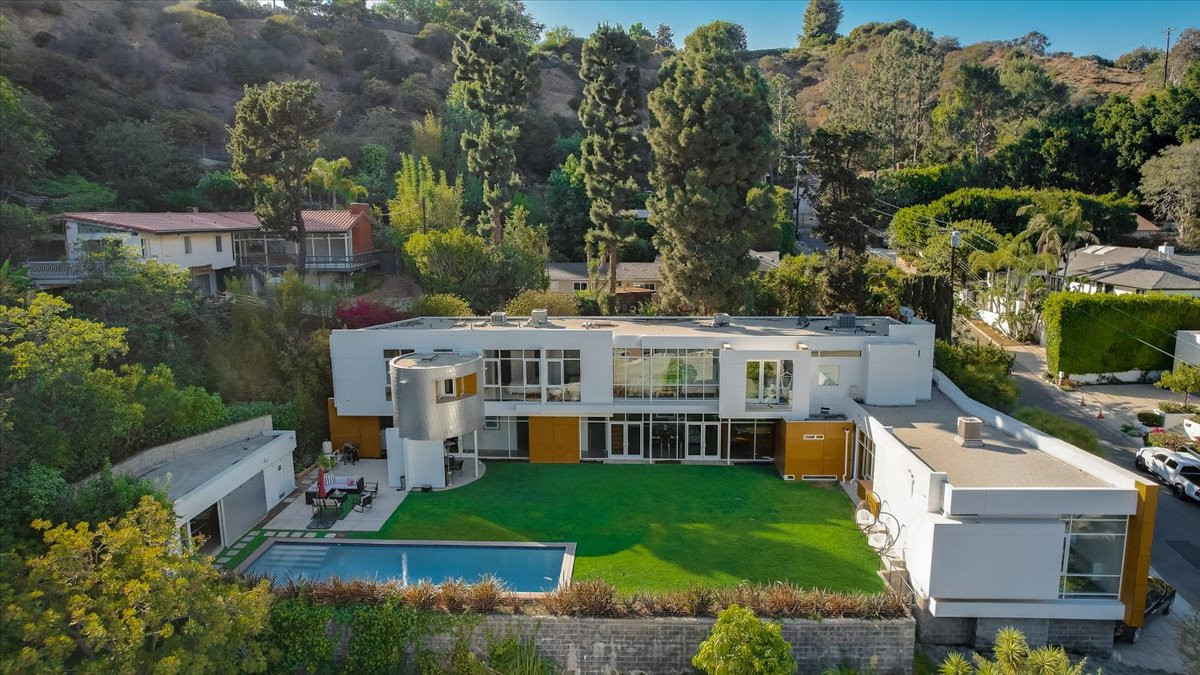 Aerial view of modern Beverly Hills estate featuring a large backyard lawn, rectangular pool, and hillside surroundings.